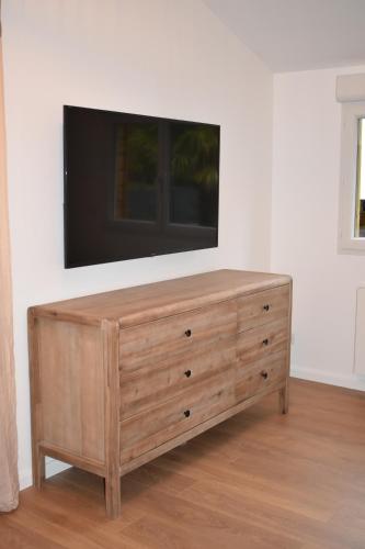 uma cómoda em madeira com uma televisão de ecrã plano na parede em Au Bord de l'Oise em Auvers-sur-Oise