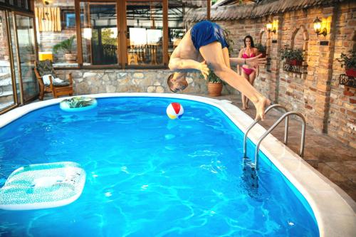 a man jumping into a swimming pool with a ball at Etno Vila Kula in Malo Središte