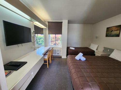 a small room with a bed and a desk with a television at Hume Inn Motel Albury CBD in Albury