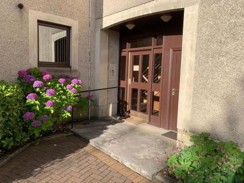 a door to a building with flowers in front of it at Teith court apartment with private parking. in Stirling