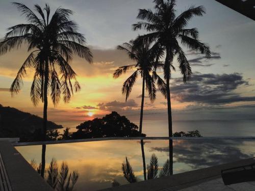 two palm trees in front of a pool with a sunset at AV Suites in Puerto Galera