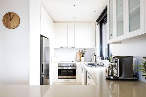 a kitchen with white cabinets and a clock on the wall at Iconic Mid-century modern, waterfront apartment in Geelong