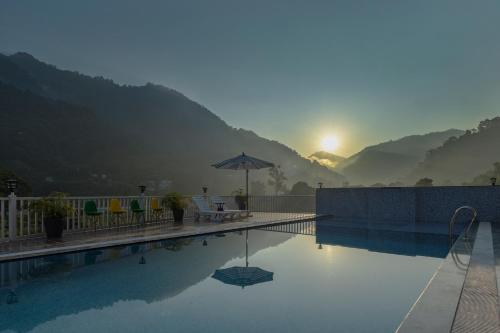a swimming pool with the sun setting in the mountains at Zostel Plus Rishikesh, Mohanchatti in Rishīkesh