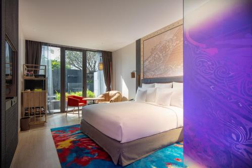 Hotel Indigo Phuket Patong, an IHG Hotel في شاطيء باتونغ: غرفة نوم بسرير ابيض كبير وغرفة بها نافذة
