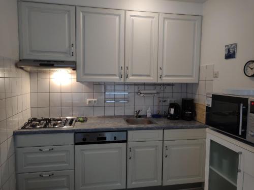 a kitchen with white cabinets and a sink and a microwave at AMPEL Bed by the Sea in Westkapelle