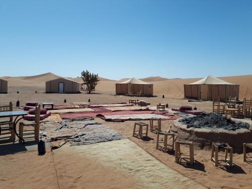 un camp dans le désert avec des tables, des chaises et des tentes dans l'établissement Auberge la Palmeraie, à M'Hamid El Ghizlane