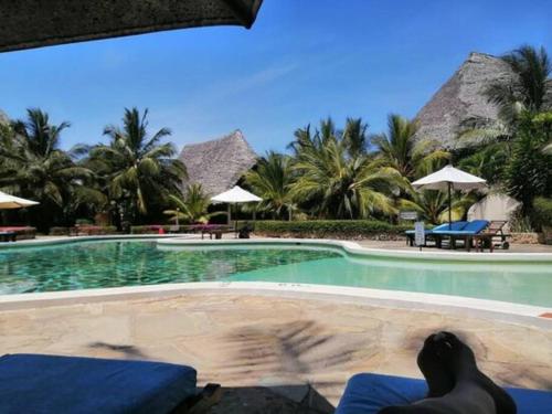 a person laying on a chair in front of a swimming pool at Tembo Baharini Beach Cottage in Malindi