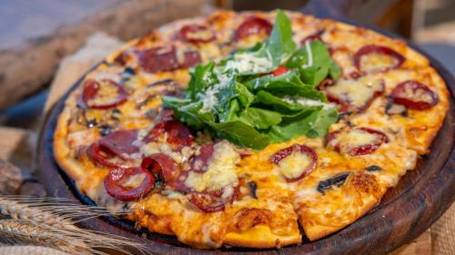 a pizza on a wooden plate with greens on it at Azka Hotel in Bodrum City