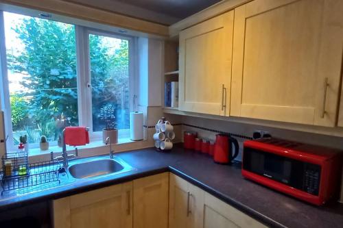eine Küche mit einer Spüle und einer roten Mikrowelle in der Unterkunft Peaceful 4 bedroom house with free parking in Frimley