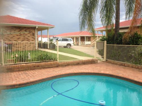 a swimming pool in front of a house with a fence at Baybrook Motor Inn in Muswellbrook
