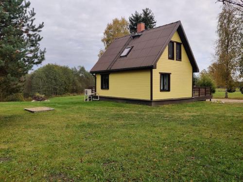 a yellow house with a black roof on a field at Ilvese Cottage Lintsi jõe kaldal in Änari