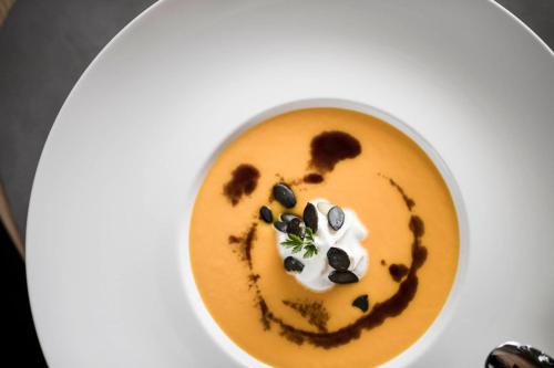 a white plate with a bowl of soup with whipped cream at Alpinhotel Vajolet - Adults only in Tires