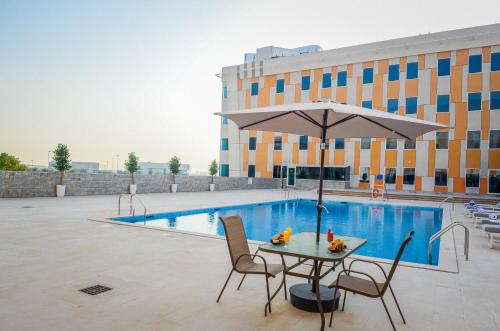 Best Western Plus Dubai Academic City في دبي: طاولة مع مظلة بجوار حمام السباحة