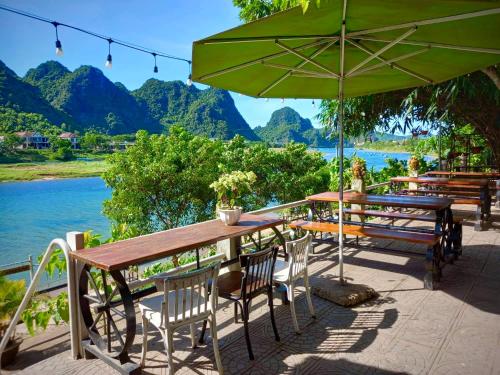 a wooden table and chairs with an umbrella and water at Areca Bungalow in Phong Nha