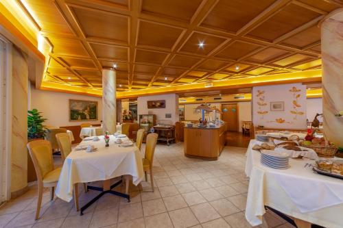 ein Restaurant mit weißen Tischen und Stühlen sowie einer Küche in der Unterkunft Frühstücks-Hotel Olympia in Dorf Tirol