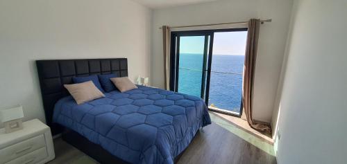 a bedroom with a blue bed and a large window at Apartamento T2-5m Aeroporto CR7 in Santa Cruz