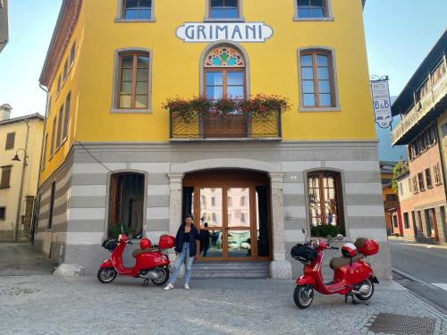 a woman standing in front of a yellow building with three scooters at Residenza d'Epoca Albergo Grimani in Ampezzo