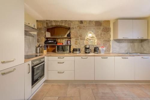 uma cozinha com armários brancos e uma parede de pedra em court séjour em Houssen