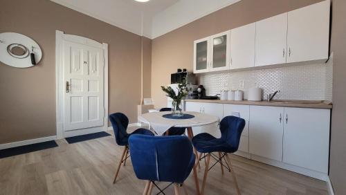 a kitchen with a white table and blue chairs at Glamour Apartman in Gyula