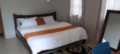 a bedroom with a large bed with white and orange sheets at Tusubira village in Jinja