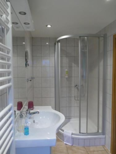 ein weißes Bad mit einer Dusche und einem Waschbecken in der Unterkunft „Frische Quelle“ Jonsdorf in Kurort Jonsdorf