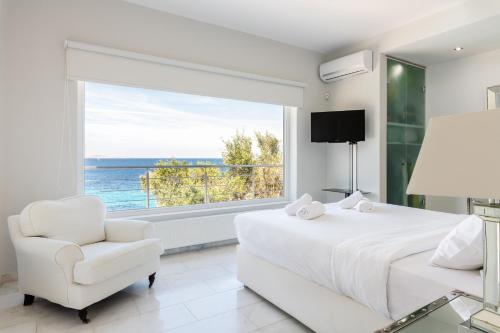 a bedroom with a white bed and a chair and a large window at Villa Deloxenia by Ethos Hospitality in Mikonos