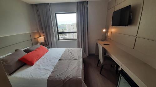 Habitación de hotel con cama, escritorio y ventana en Flat 808 moderno e privilegiada localização no Centro, en Três Rios