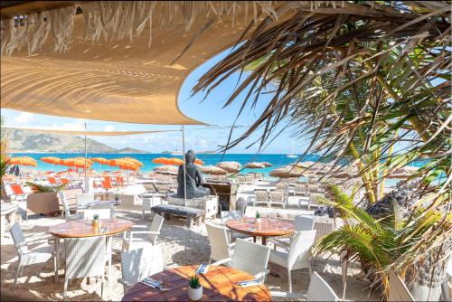 a person sitting at a beach with tables and chairs at Top floor unit 520 ft2 - 48 m2 with stunning dominant view on ocean, St Barth, Orient Bay in Cul de Sac