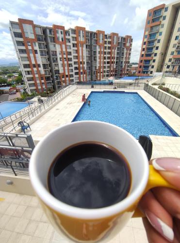 a person holding a cup of coffee next to a swimming pool at Reserva del Peñon in Girardot