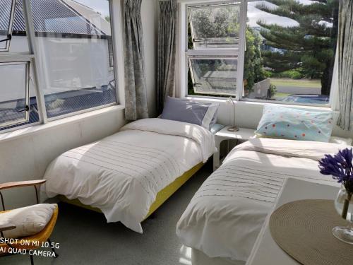 two beds in a room with two windows at Hosts on the Coast Paradise on Pipi in Whangamata