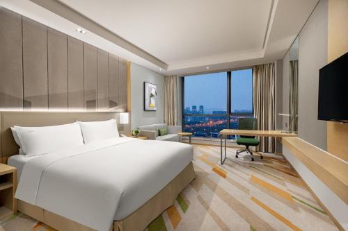 無錫市にあるHoliday Inn Wuxi Taihu New City, an IHG Hotelのベッド、デスク、窓が備わるホテルルームです。