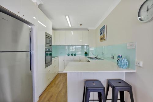 una cocina con armarios blancos y una barra con 2 taburetes en Beach Palms Holiday Apartments, en Gold Coast