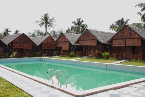 a resort swimming pool in front of a row of wooden huts at Nipoh Beach Cottage in Kijal