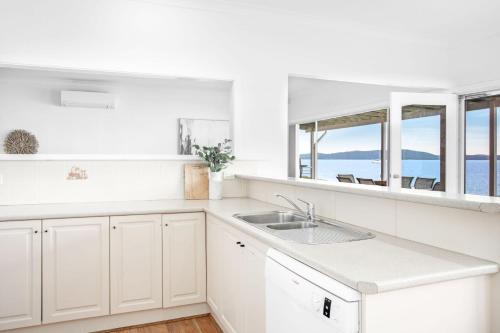 a white kitchen with a sink and a view of the ocean at Beached Inn Spacious beach front house in Salamander Bay