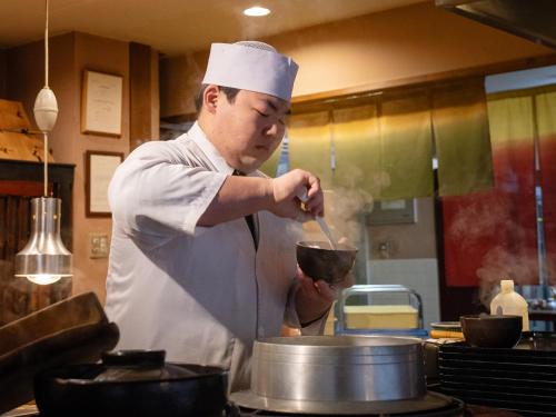 a chef stirring a pot in a kitchen at Hakkei in Maniwa