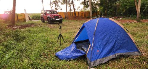 a blue tent in the grass next to a red jeep at JJ's Holiday Home in Thanniyam