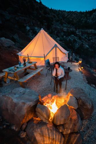 a woman sitting in a tent next to a fire at Zion Glamping Adventures in Hildale
