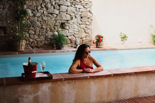 a woman sitting next to a swimming pool with a glass of wine at Demeure de la Carmine, sejour bien-etre d'exception, piscine, hammam, champagne in Mirepoix