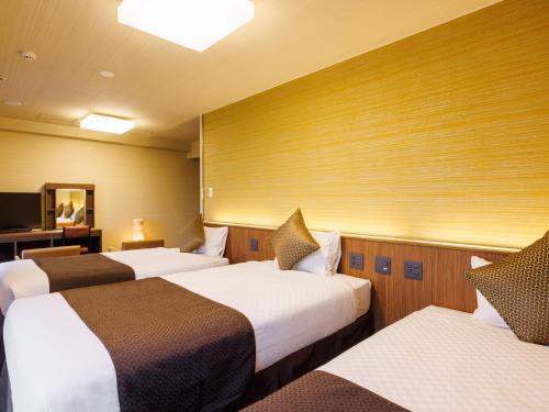 um quarto de hotel com três camas e uma televisão em KAMENOI HOTEL Yamato Heguri em Heguri