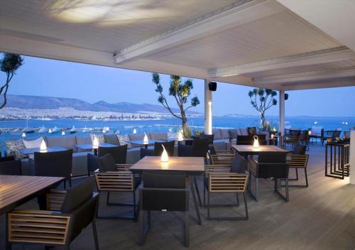 a restaurant with tables and chairs and a view of the ocean at The Alex Monte Kastella, Santikos Collection in Piraeus