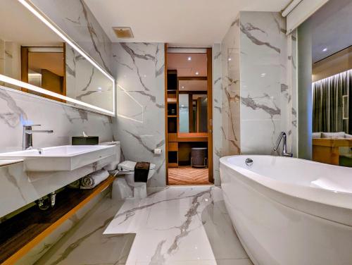 a white bathroom with a tub and a sink at Grand Zuri Lubuklinggau in Lubuklinggau