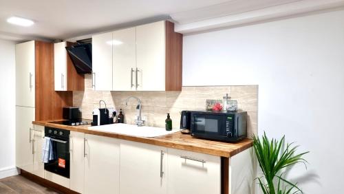 uma cozinha com armários brancos, um lavatório e um micro-ondas em Thompson Apartments by Switchback Stays em Cardiff