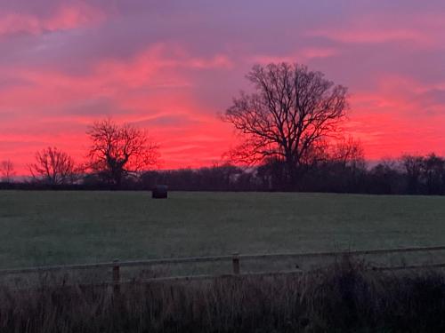 a sunset in a field with a fence and trees at The Dragon's Hut with cozy logburner in Wrexham