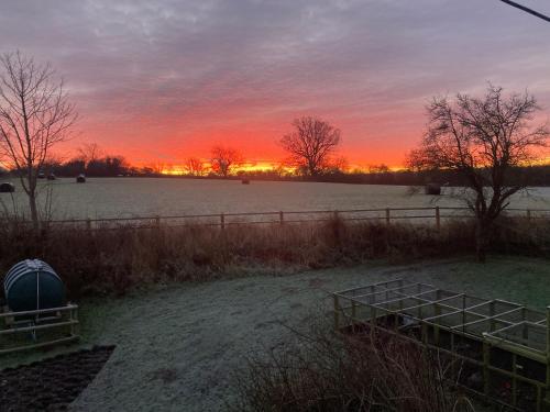 a sunset in a field with a fence and a field at The Dragon's Hut with cozy logburner in Wrexham