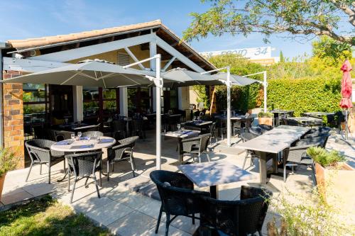 un patio al aire libre con mesas, sillas y sombrillas en The Originals City, Hôtel Le Pavillon, Béziers Est, en Béziers