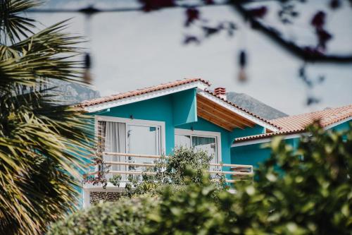 a blue house with a balcony and palm trees at Drymades Bungalows Adults Only in Dhërmi