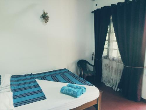 a bedroom with a bed with blue sheets and a window at Kasun Hotel in Koslanda