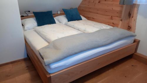 ein Holzbett mit weißer Bettwäsche und blauen Kissen in der Unterkunft Almchalet Schuster in Diex