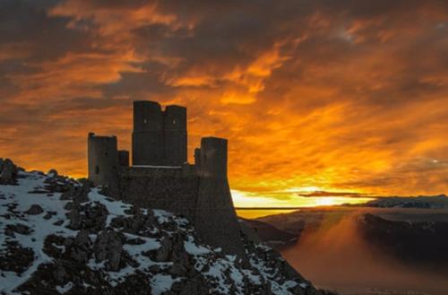 ein Schloss auf einem verschneiten Berg mit Sonnenuntergang in der Unterkunft Damuz house in Calascio