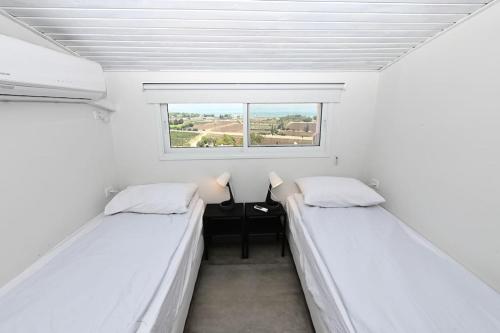 two beds in a small room with a window at Gluck House in Migdal